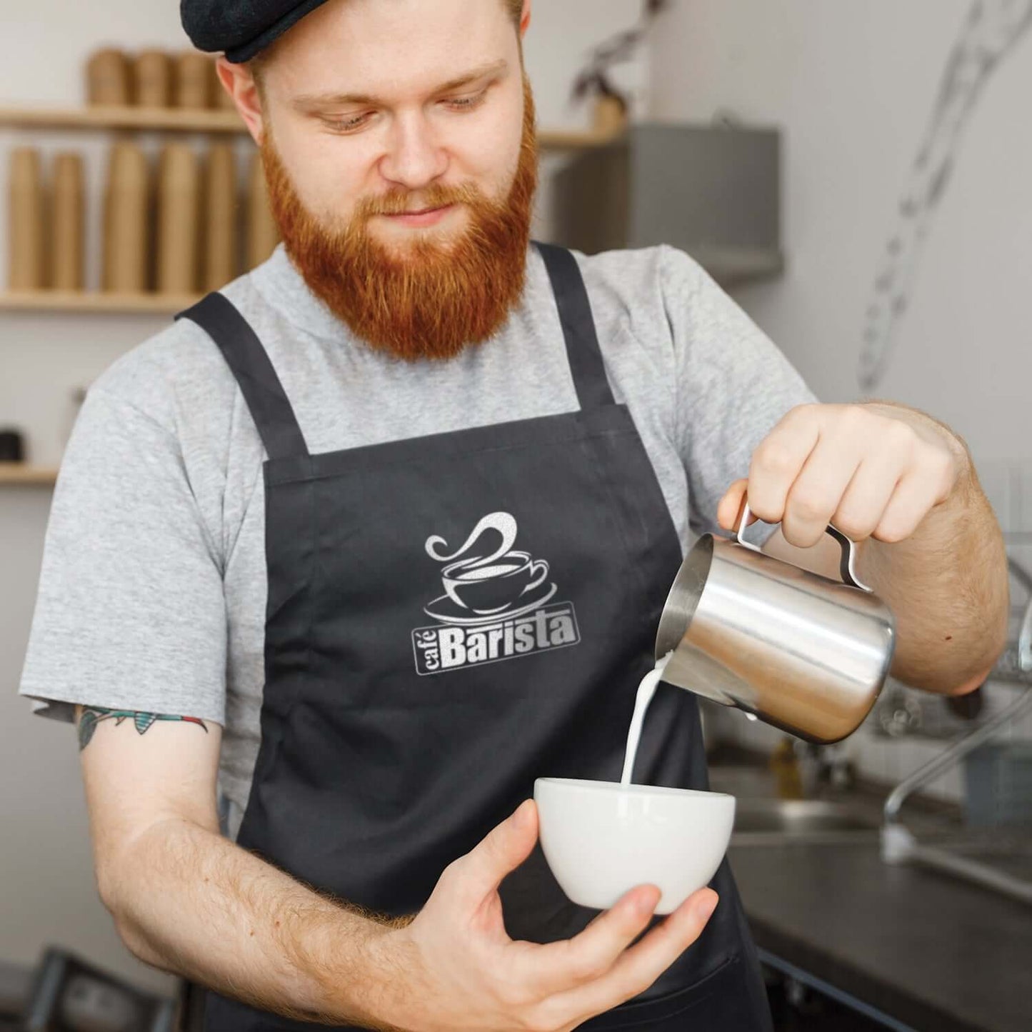 Barista wearing Savoy Bib Apron, pouring milk into a bowl, showcasing functionality in a café setting.