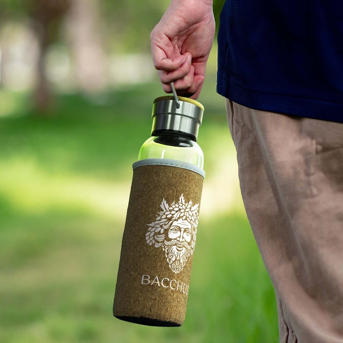 Person holding a Nomad Glass Bottle with Cork Sleeve featuring a natural cork cover and carry handle.