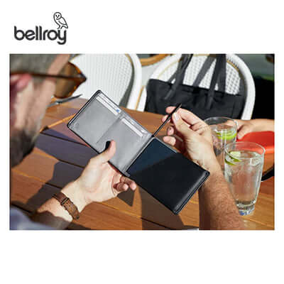Person using Bellroy Micro Pen with a travel wallet at an outdoor table, perfect for corporate gift ideas.