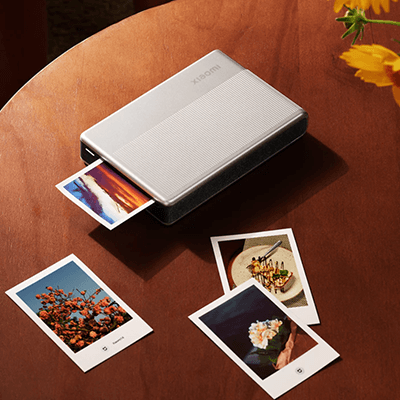 Xiaomi Portable Photo Printer 1S printing photos on a wooden table surrounded by printed memories.