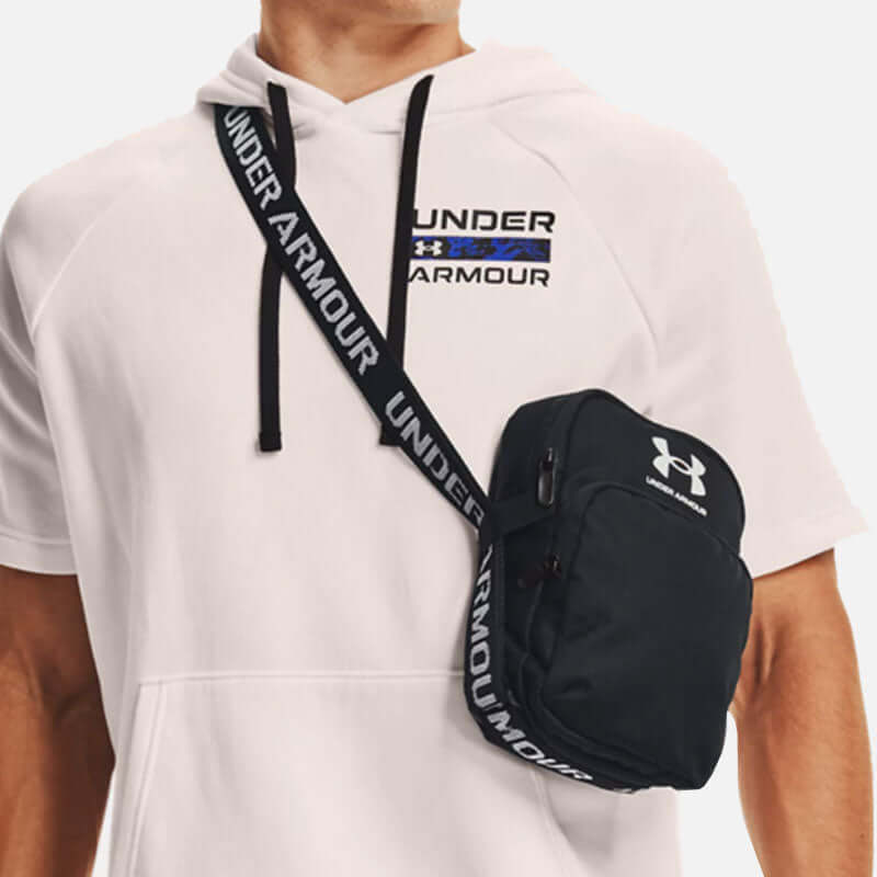 Under Armour Loudon Crossbody Bag worn by a model in a hoodie, showcasing its sleek black design and adjustable strap.