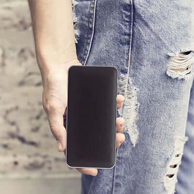 Person holding a smartphone with a blank screen, wearing ripped jeans.