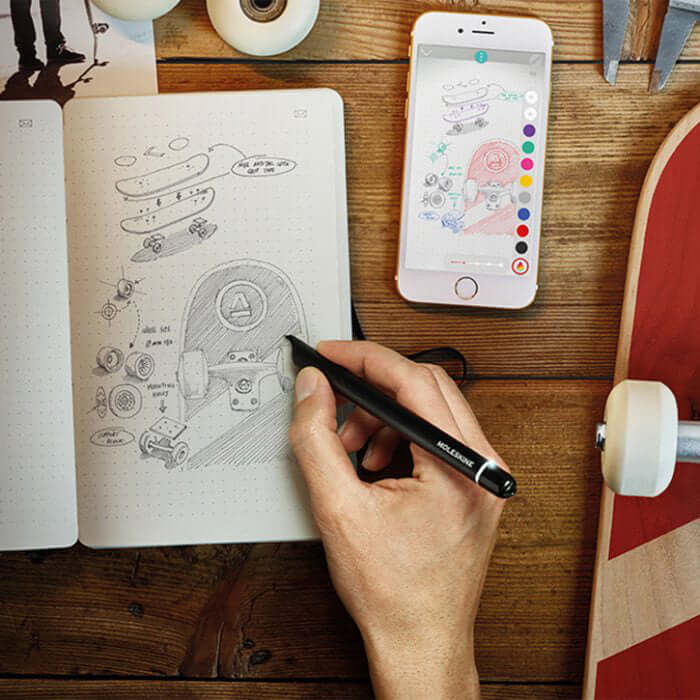 Hand using MOLESKINE Smart Writing Set to sketch in notebook while smartphone displays digital version.