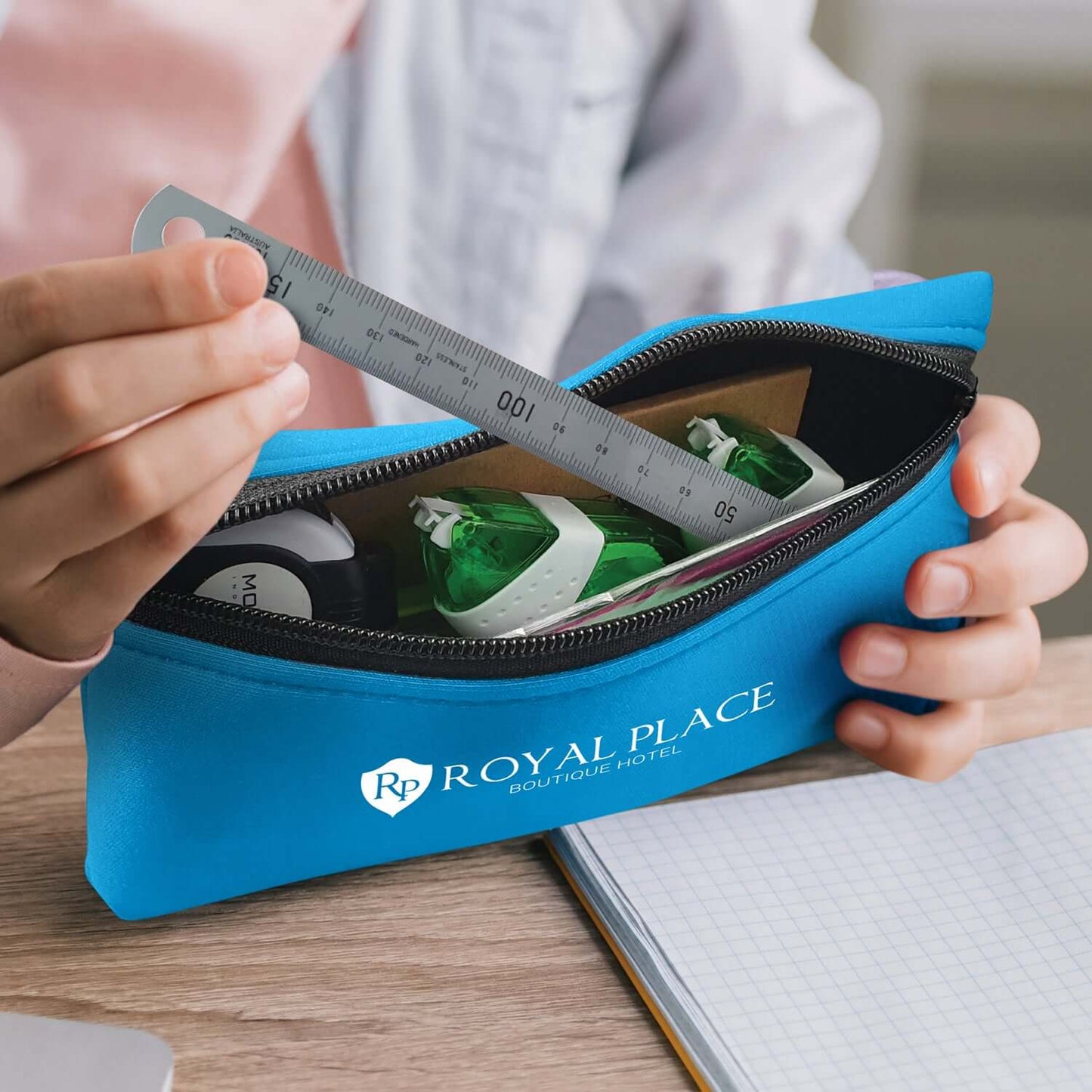 A person holding a blue Puma Pencil Case filled with stationery, featuring the logo of Royal Place Hotel.