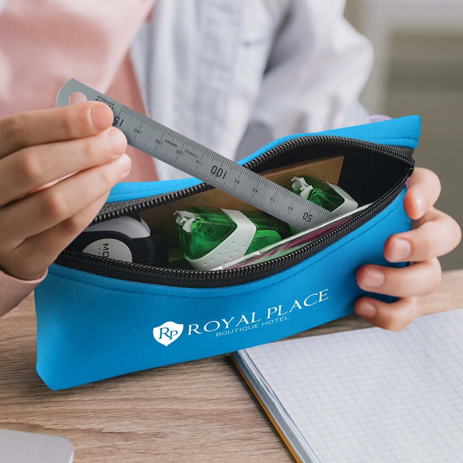 A person holding a blue Puma Pencil Case filled with stationery, featuring the logo of Royal Place Hotel.