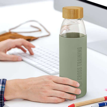 Person holding a Solstice Glass Bottle with bamboo lid and silicone sleeve, ideal as a corporate gift.