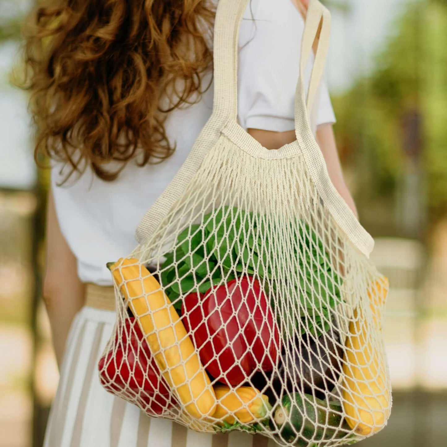A woman holding a Cotton Mesh Foldaway Tote Bag filled with fresh fruits and vegetables.