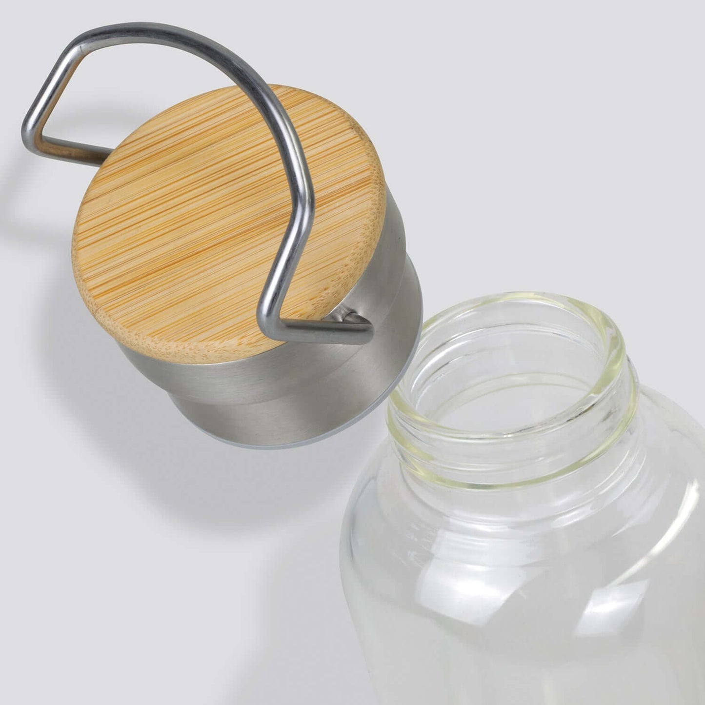 Nomad Glass Bottle close-up showing bamboo lid and stainless steel handle for a stylish and secure hydration solution.