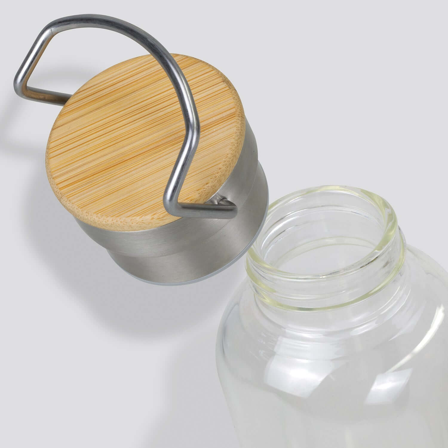 Nomad Glass Bottle close-up showing bamboo lid and stainless steel handle for a stylish and secure hydration solution.