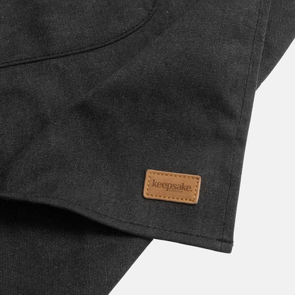 Close-up of the Keepsake Canvas Apron showcasing the leather-look label on the chic washed black fabric.
