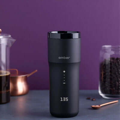 Ember Travel Mug 2 12oz displayed on a table with coffee accessories, showcasing its touch display and sleek design.