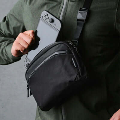 Person holding a Nintendo Switch with ALPAKA Flight Sling Axoflux 200D bag for convenient carrying.