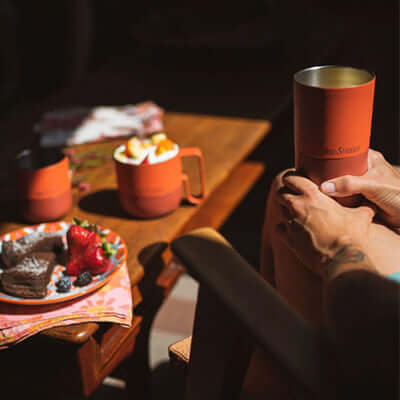 Klean Kanteen Rise 16oz Tumbler (with Flip Lid) held by person with dessert and drinks on a table.