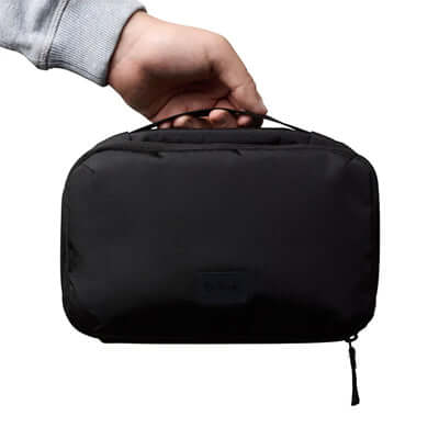 A hand holding the Bellroy Hanging Toiletry Kit, a sleek black travel case for organization.