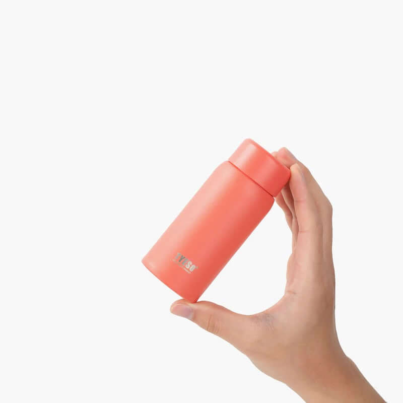 Hand holding TYESO Mini Pocket Bottle 5oz in coral color, ideal for hydration and as a corporate gift.