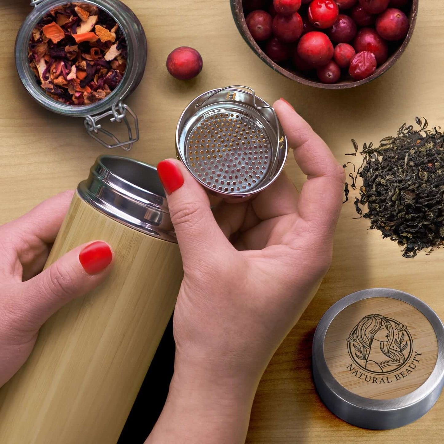 User holding NATURA Bamboo Vacuum Bottle with a tea infuser, surrounded by dried fruits and herbs.