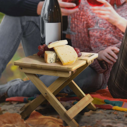 NATURA Bamboo Folding Wine Table holding cheese and wine in an outdoor setting, perfect for a picnic or corporate gift.