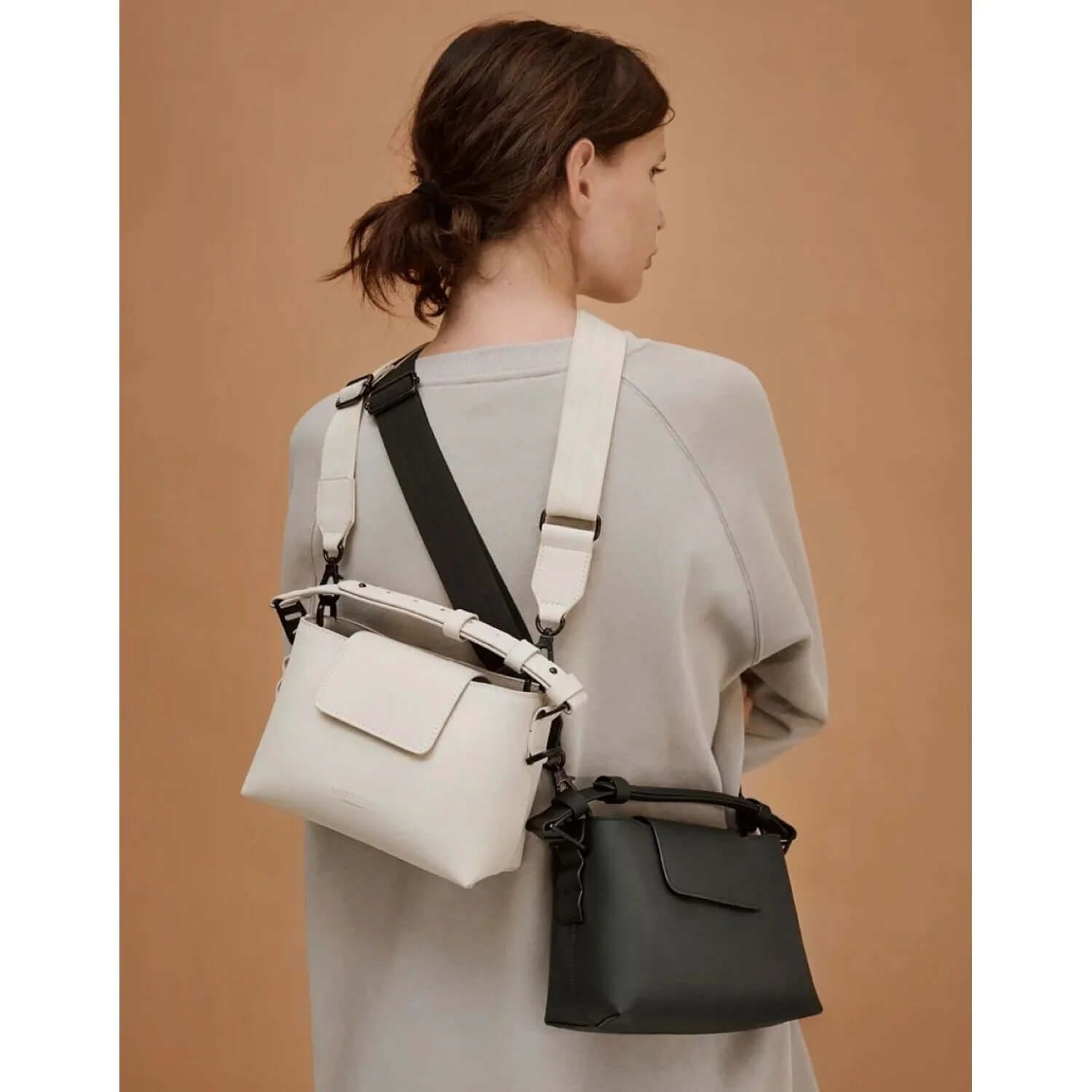 Woman wearing Gaston Luga Splashini Crossbody bags in white and black, showcasing adjustable straps.