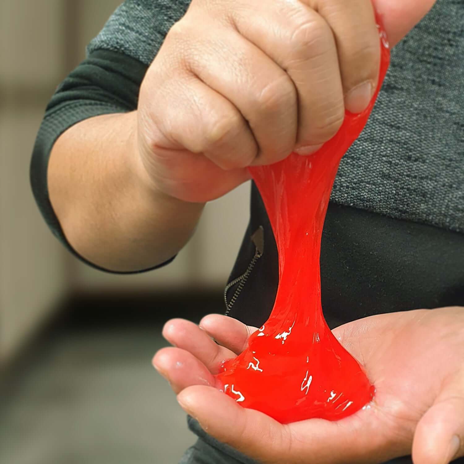 A person squeezing bright red Stress Slime in their hands, showcasing the fun and stress-relieving qualities of the product.