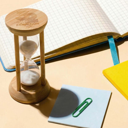 Tempus Bamboo Hourglass on a desk beside a notebook, paper, and a paperclip for corporate gift ideas.