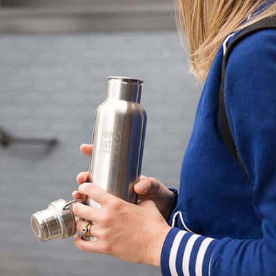 Person holding Klean Kanteen Insulated Reflect Stainless Steel Bottle outdoors, showcasing its sleek design and eco-friendly materials.