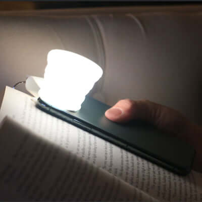 BrandCharger Smartphone Lumi Lightbulb illuminating a book in low light, perfect for reading and as a corporate gift.