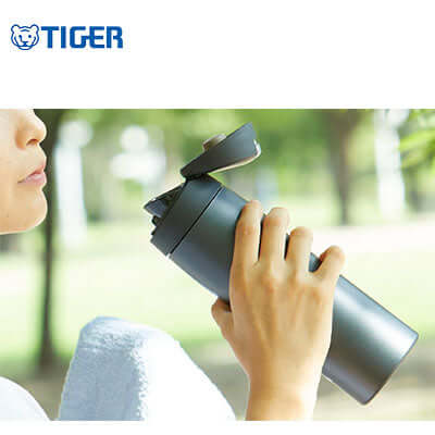 User holding the Tiger Flip Cap Stainless Steel Thermal Bottle MJE-A outdoors, featuring its easy-open cap.