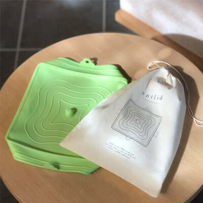 Storage Lid Set in green silicone on a wooden surface with a cotton storage bag.