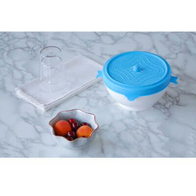 Storage Lid Set on a marble countertop next to a bowl of fruit and glasses, perfect for keeping food fresh.
