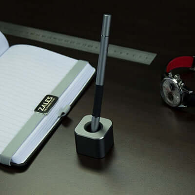 BrandCharger Qube Elegant Aluminium Apple Pencil Holder with pen on a desk next to a notebook and watch.