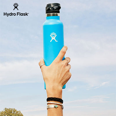 HydroFlask 21oz Standard Mouth Bottle with Sport Cap held in hand against a blue sky.