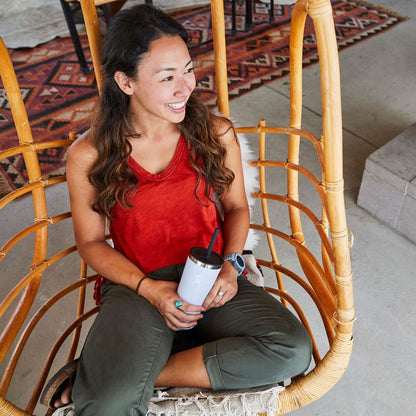 A smiling woman enjoying her HydroFlask 22oz Tumbler while sitting in a stylish hanging chair.